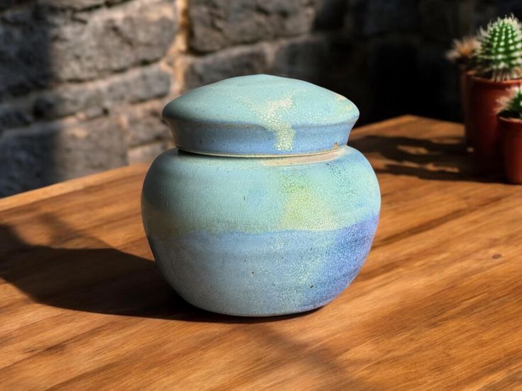 a blue vase sitting on top of a wooden table next to a potted plant