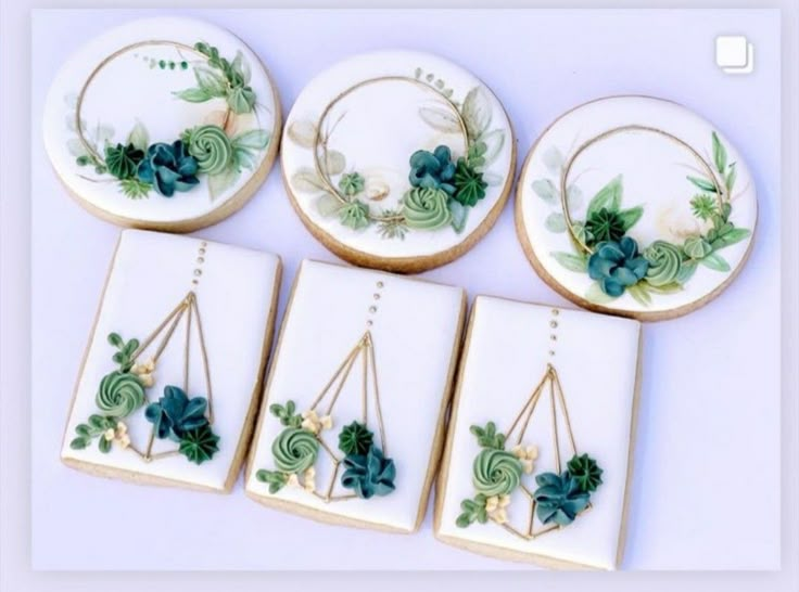 four decorated cookies sitting on top of each other in front of white plates with green plants