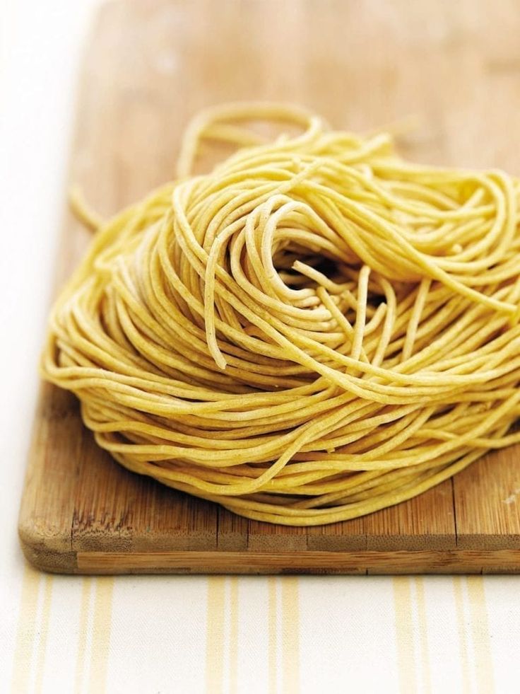 a wooden cutting board topped with lots of yellow pasta noodles on top of a table