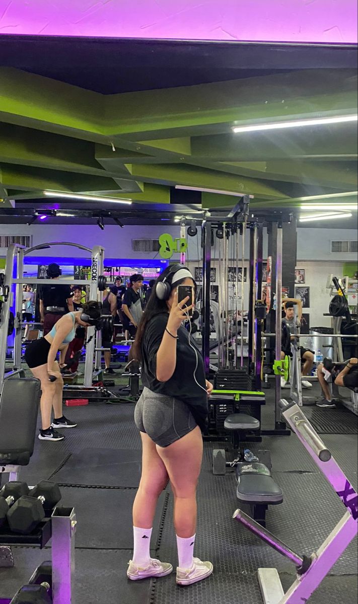 a woman standing in front of a gym machine talking on her cell phone while wearing headphones