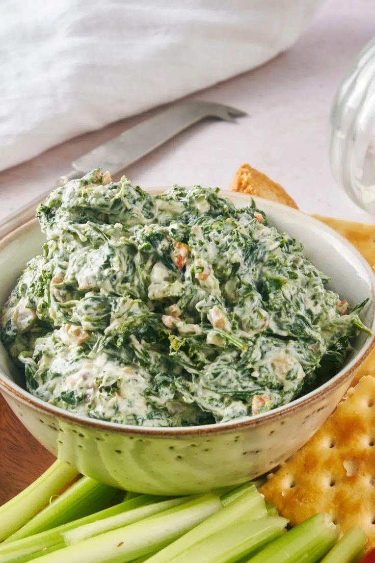 a bowl filled with spinach dip surrounded by crackers