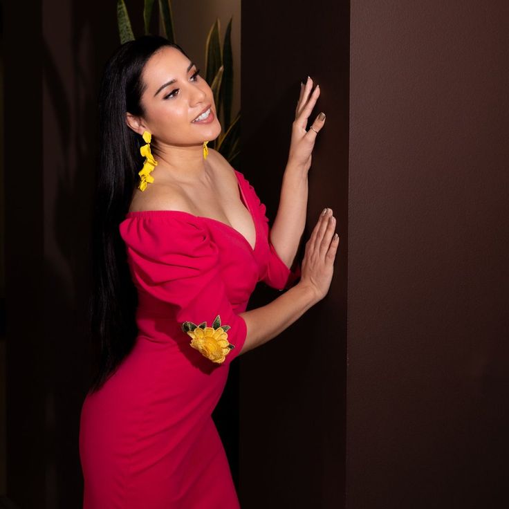 a woman in a red dress leaning against a wall with her hand up to the side