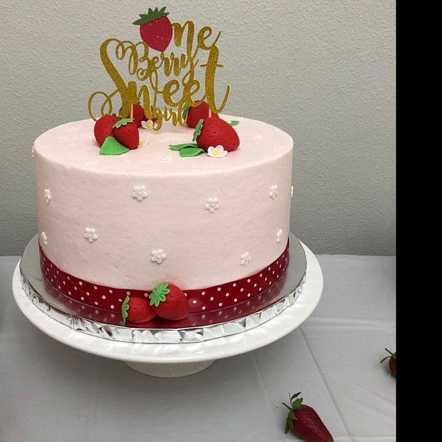 a pink cake with strawberries on top and the words happy birthday spelled in gold