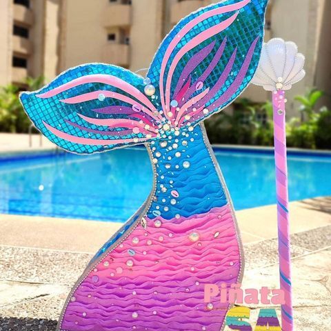 a colorful mermaid tail sculpture next to a swimming pool with a pink and blue umbrella