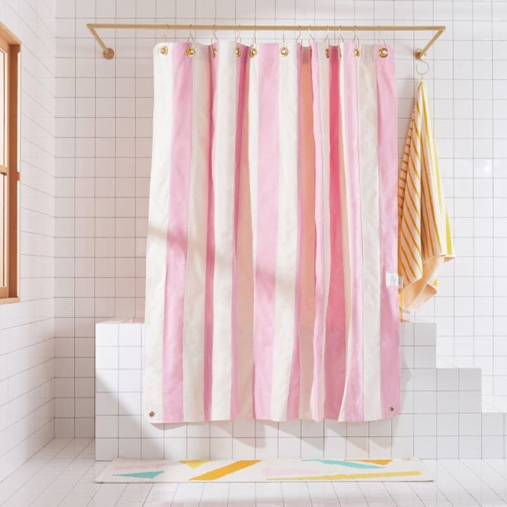 a pink and white striped shower curtain hanging from a rail in a bathroom with tiled flooring