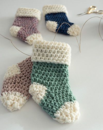 three crocheted mittens sitting on top of a table next to scissors and thread