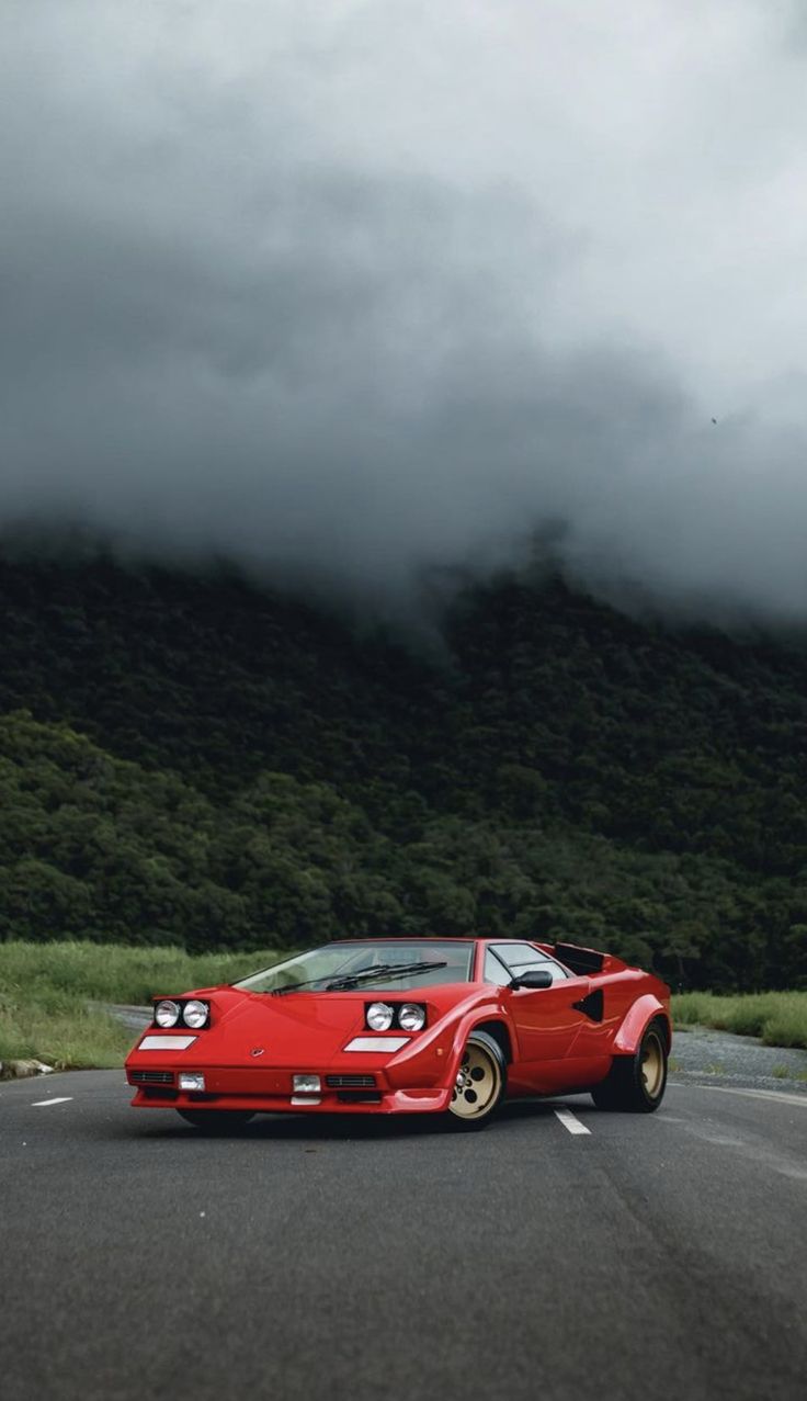 a red sports car is driving down the road in front of some mountains and clouds