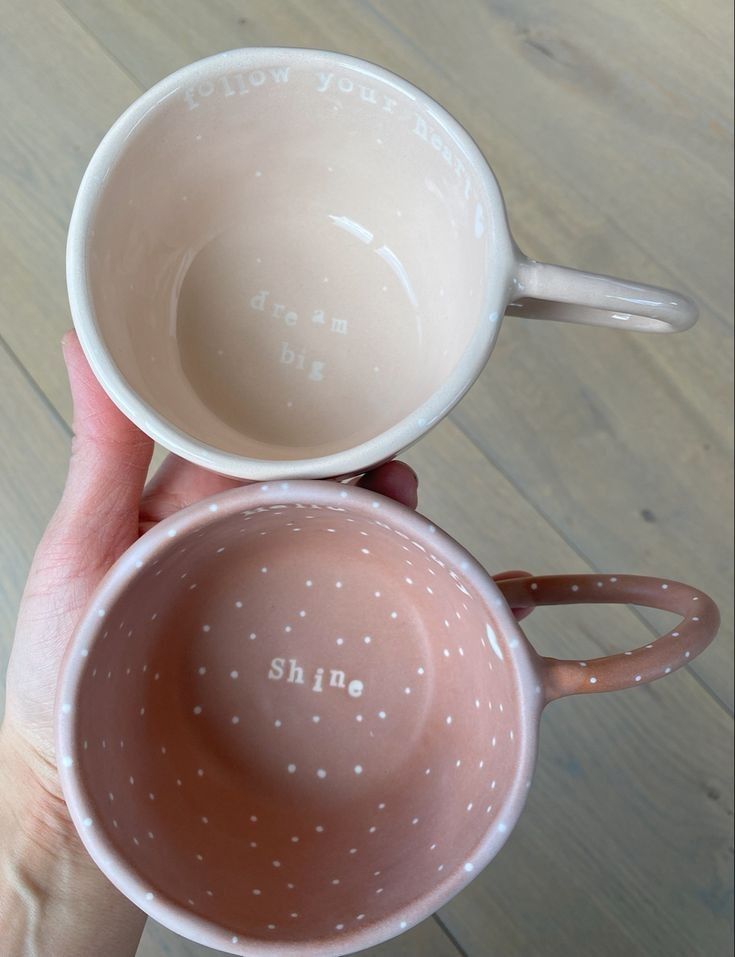 two coffee mugs with the words shine written on them are held in front of each other