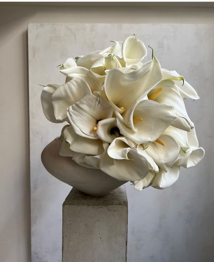 a vase filled with white flowers sitting on top of a cement block in front of a wall