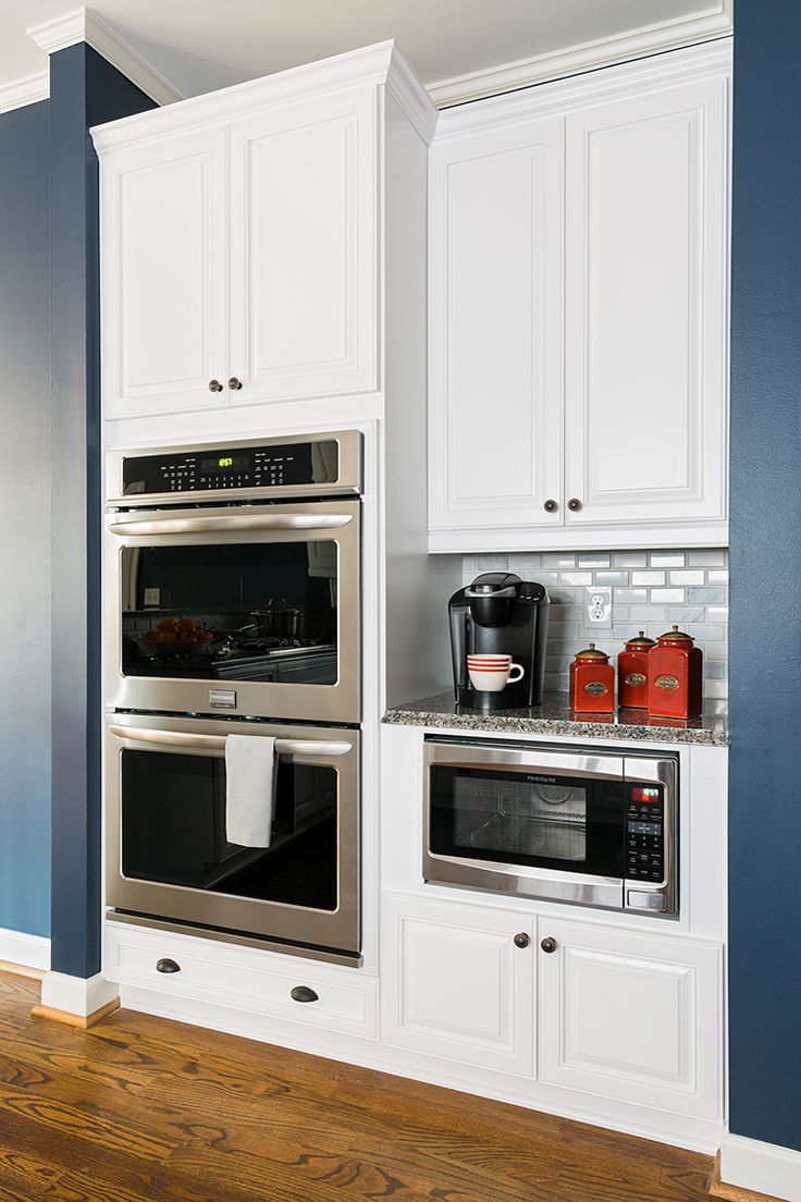 a kitchen with white cabinets and stainless steel ovens, wood flooring and blue walls