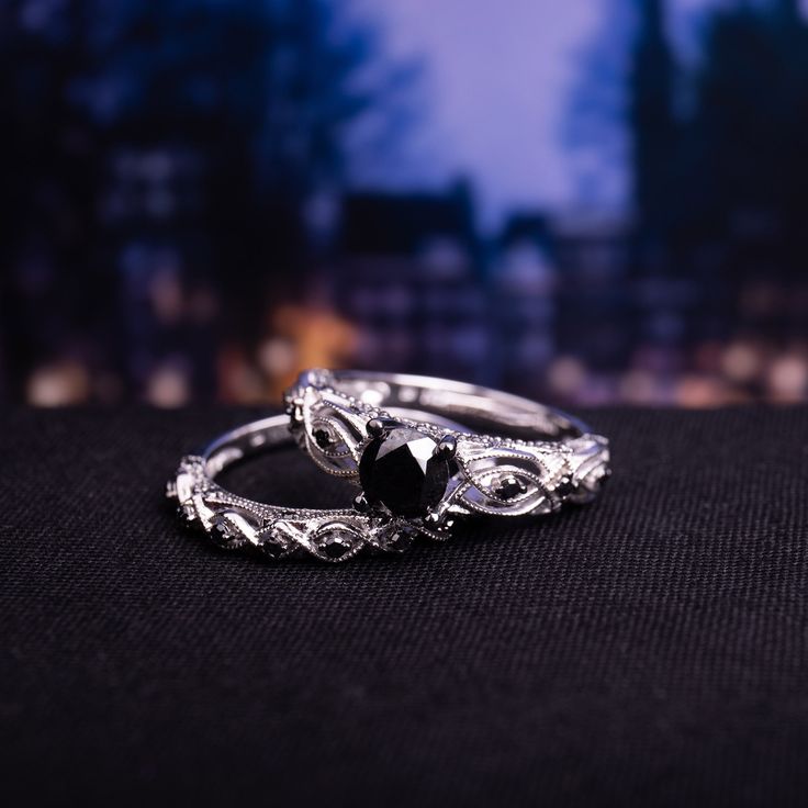 two wedding rings sitting on top of a black cloth covered table with buildings in the background