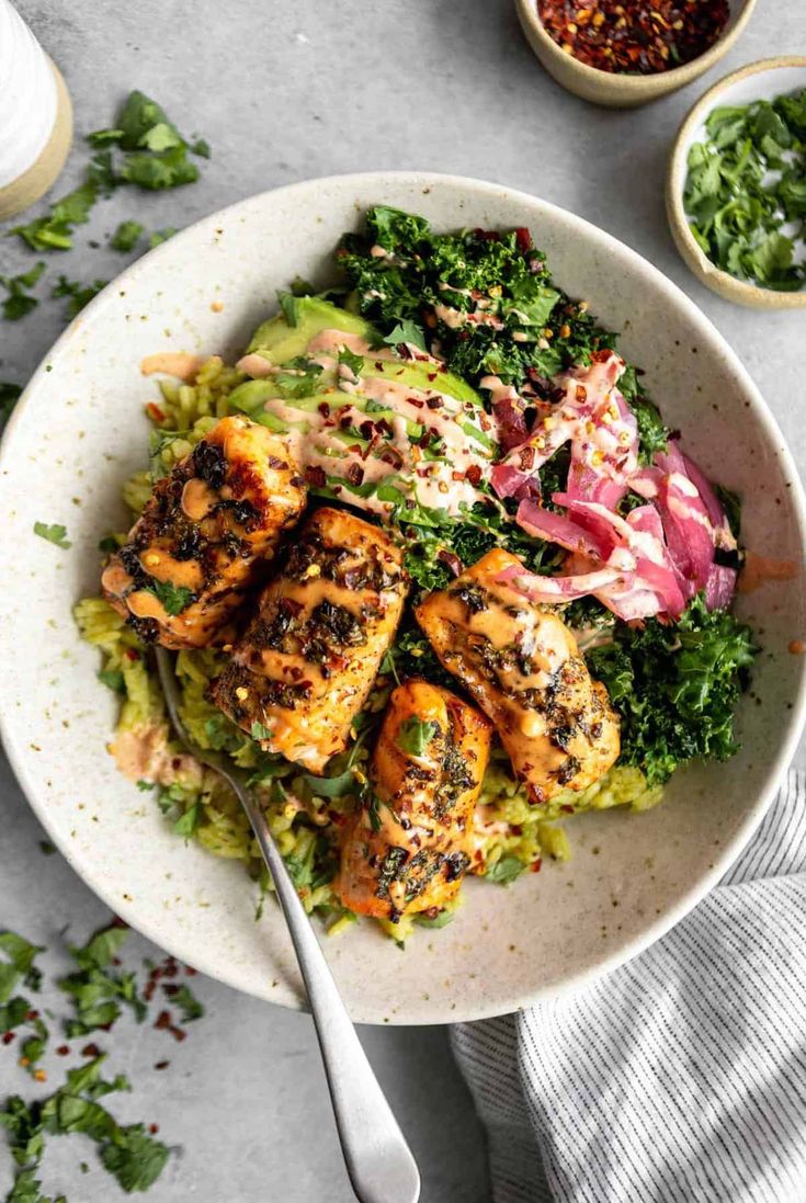 a white bowl filled with chicken, lettuce and red onion salad next to two bowls of dressing