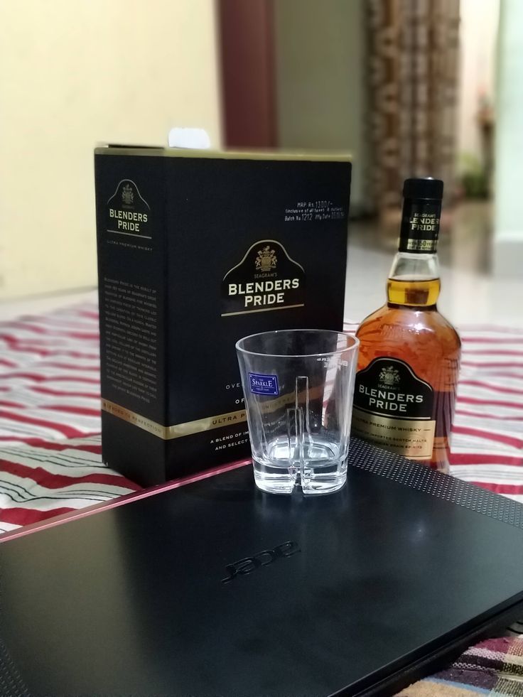 a bottle of whisky next to two glasses on a table with a laptop and notebook