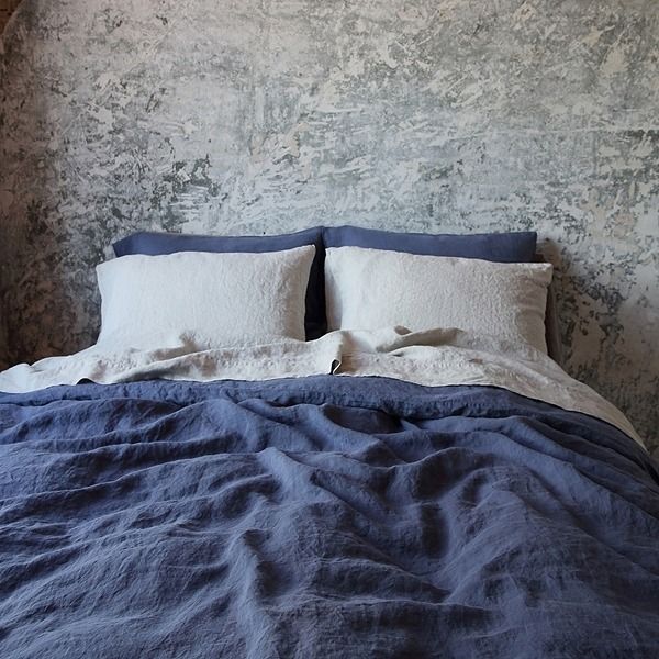 an unmade bed with blue linens and white pillows against a wallpapered background