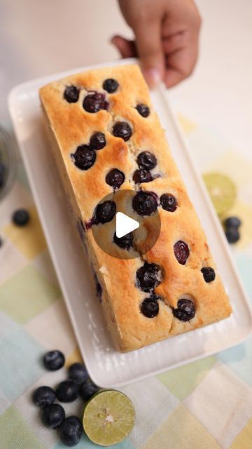 a person holding a piece of bread with blueberries on it and lemon slices around it