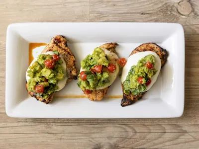 three grilled fish topped with guacamole and salsa on a white plate