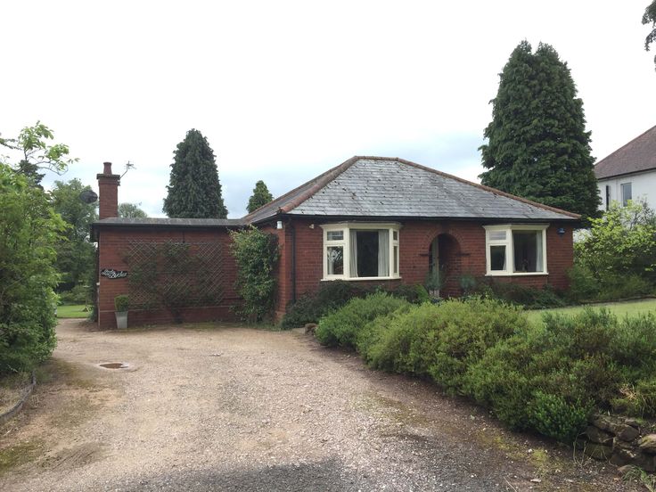 a brick house sitting next to a lush green forest filled with lots of trees and bushes