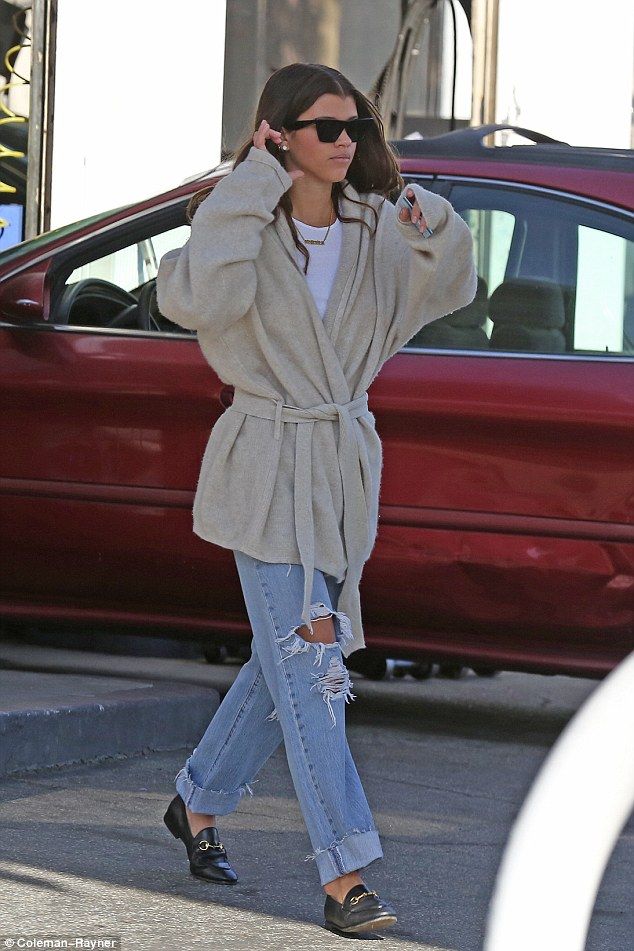 a woman in ripped jeans is talking on her cell phone while walking down the street