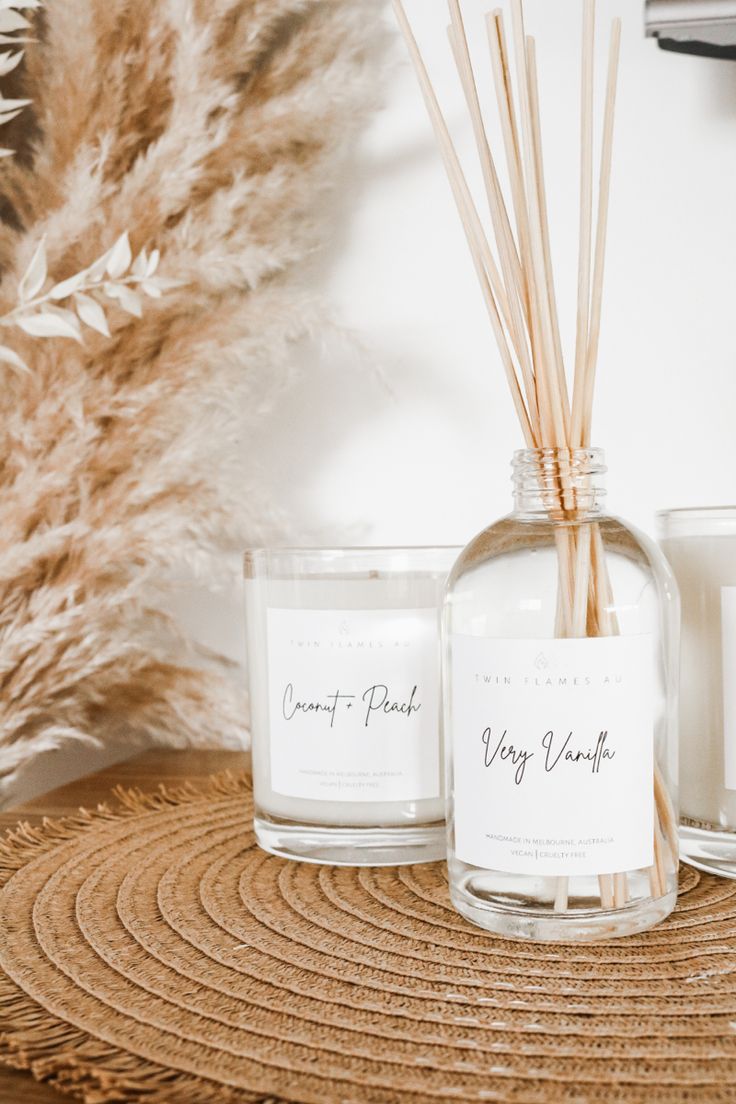 two candles sitting next to each other on top of a wooden table with dried grass