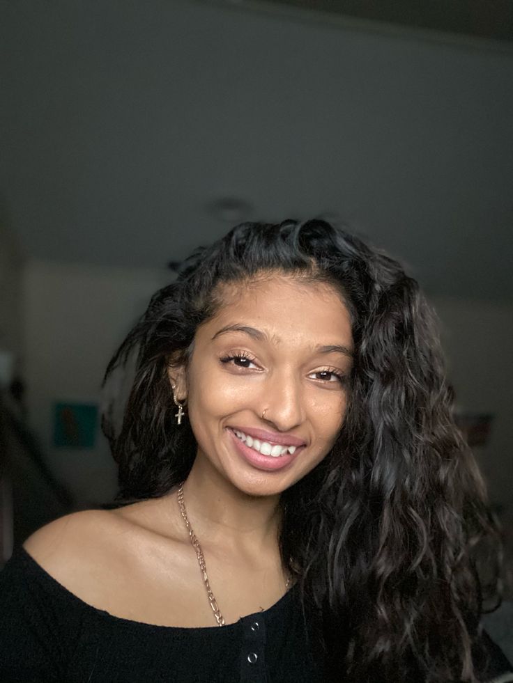 a woman with long black curly hair smiling at the camera and looking into the camera