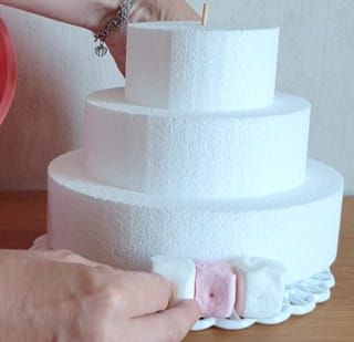 a woman is decorating a three tiered cake with pink icing on it