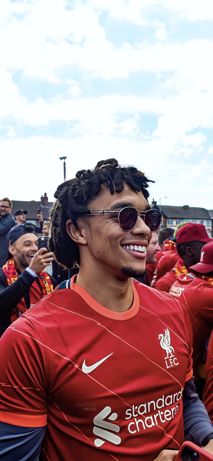 a man with dreadlocks and sunglasses standing in front of other people wearing red shirts