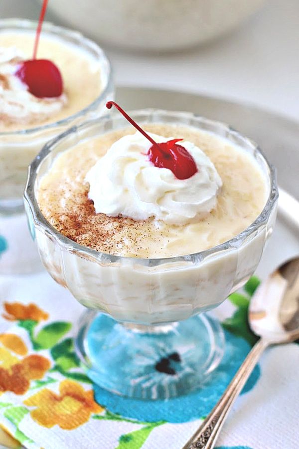 two desserts with whipped cream and cherries in small glasses on a floral napkin