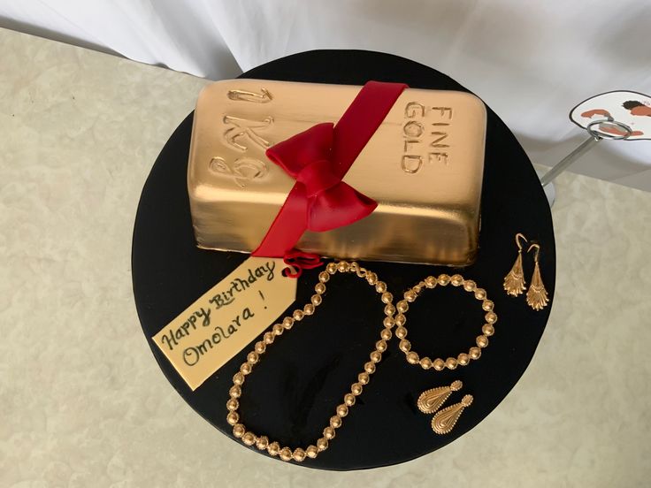 a cake decorated with gold and jewelry on top of a black platter that says happy birthday, one of a kind