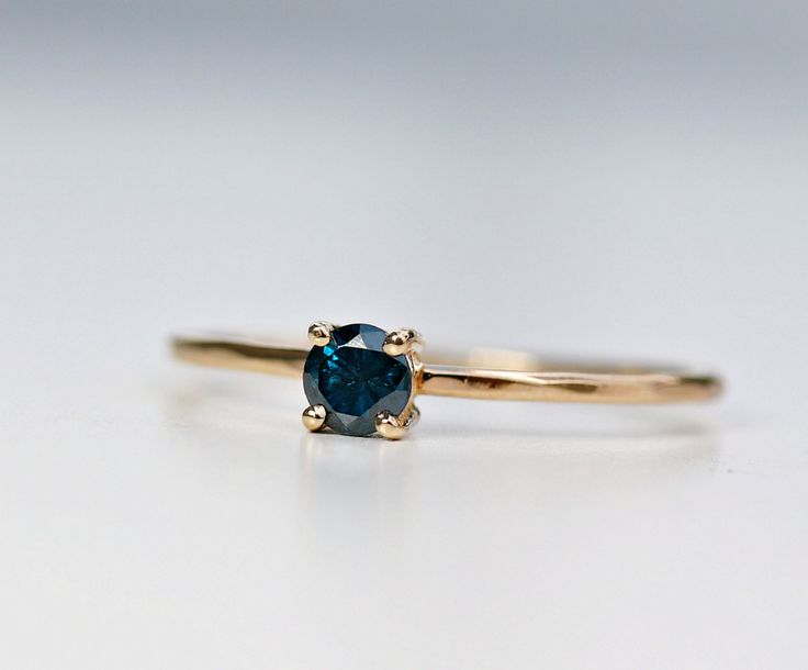 a blue diamond ring sitting on top of a white surface with a gold band around it