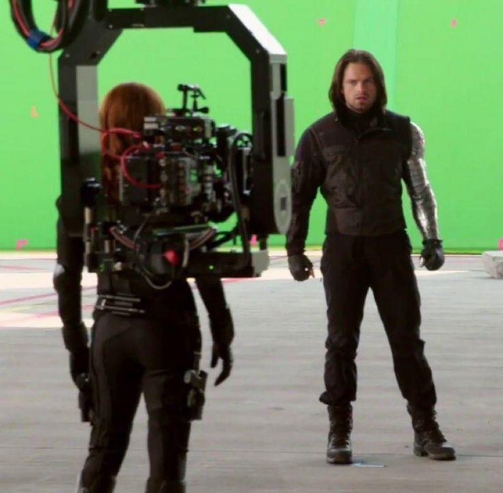 a man standing next to a camera in front of a green screen with another person behind him