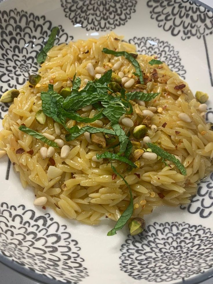 a white and blue plate topped with pasta and garnished with green leafy herbs