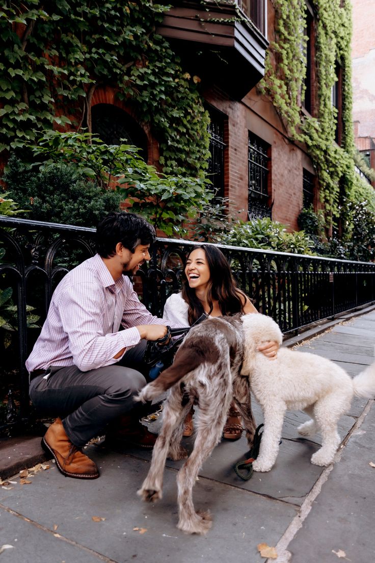 a man and woman petting two dogs on the sidewalk