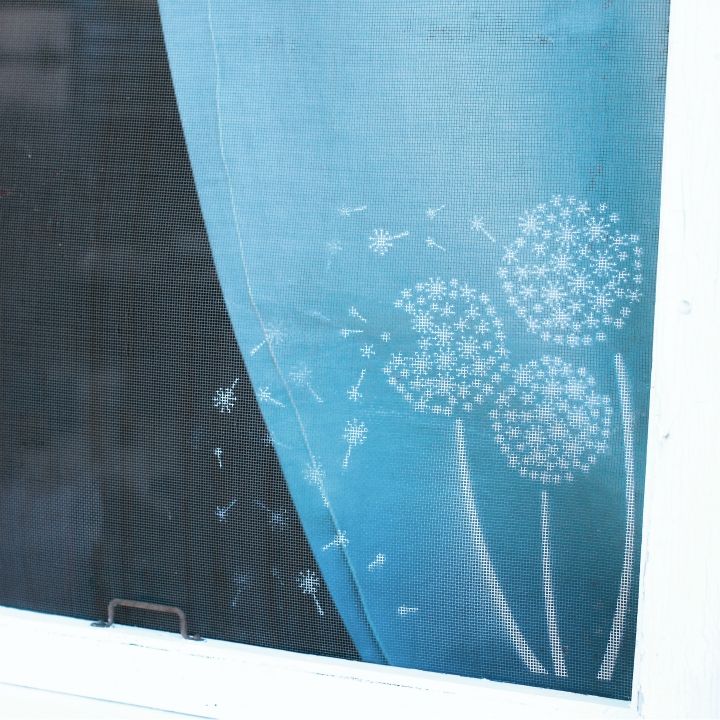 a dandelion drawn on the side of a window sill with blue curtains