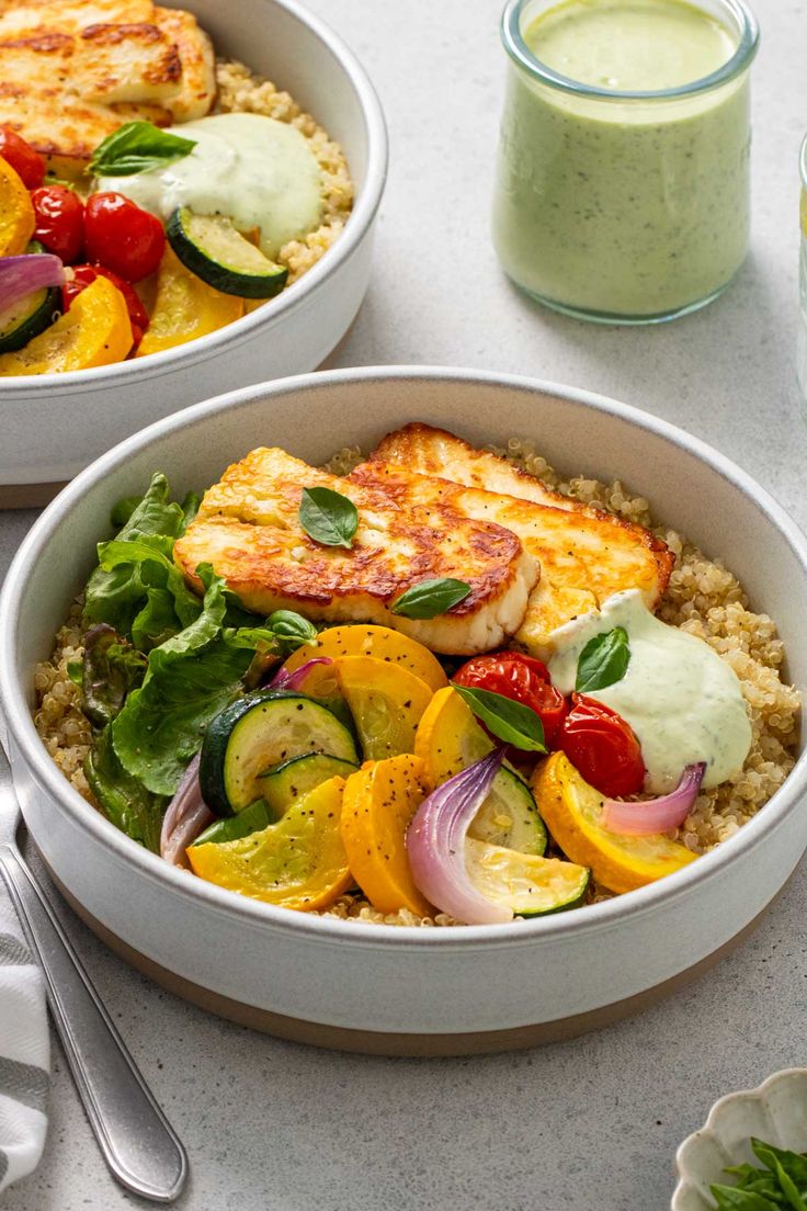 two white bowls filled with food next to a glass of green smoothie and spoons