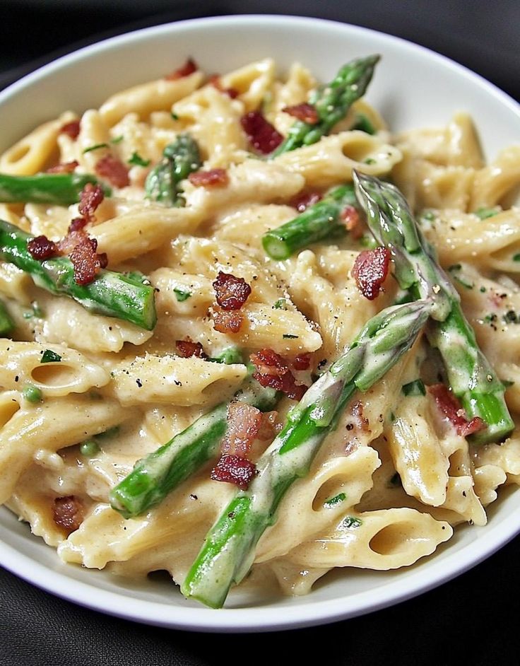 a white bowl filled with pasta and asparagus on top of a black table