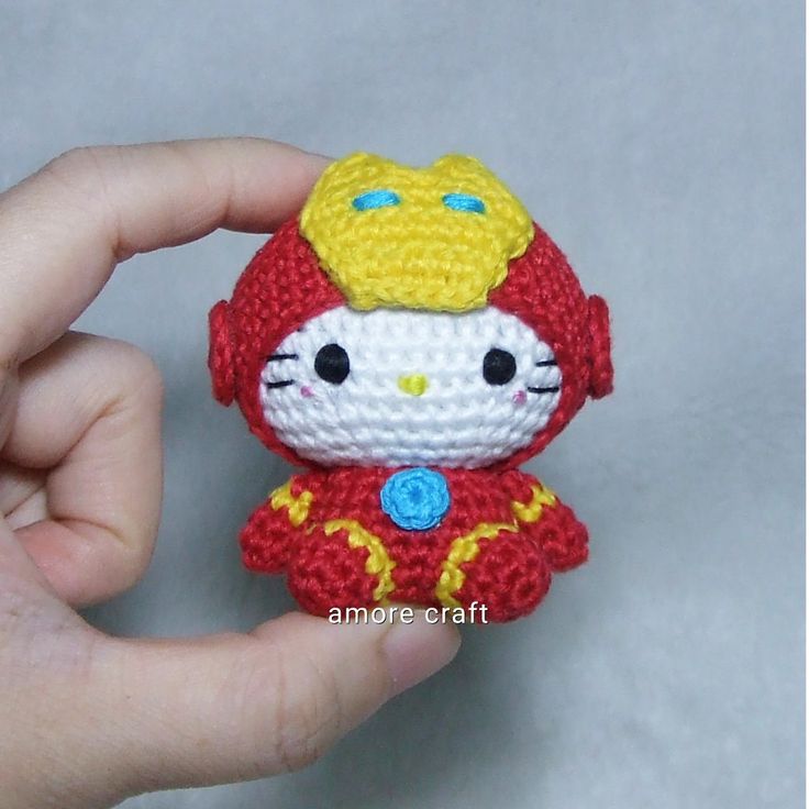 a hand holding a small crocheted hello kitty doll in red and yellow outfit