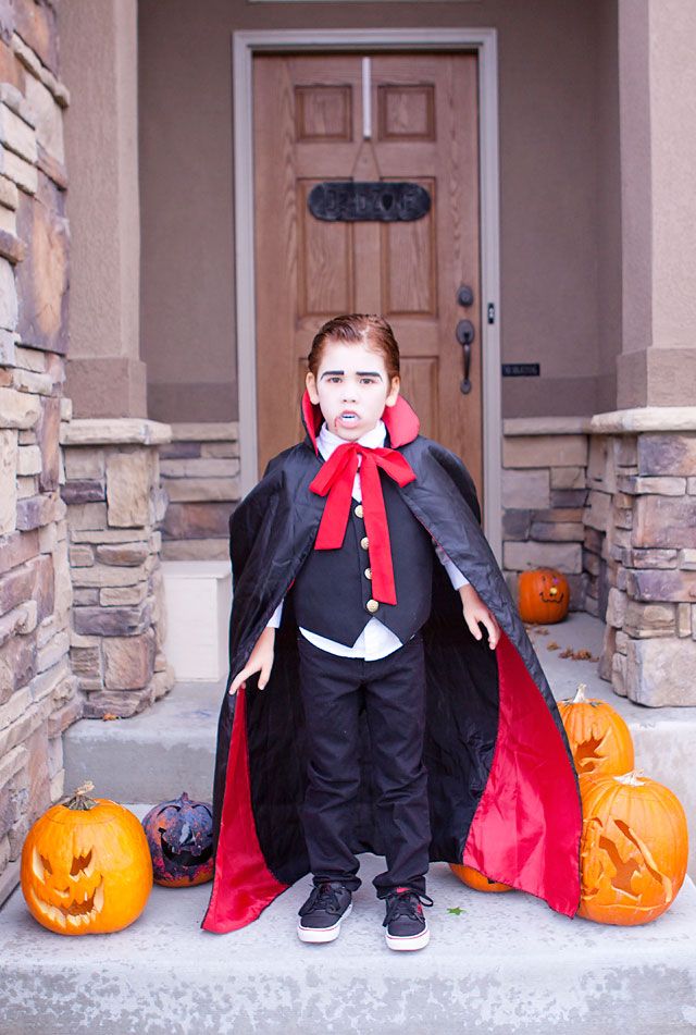 a young boy dressed as dracula standing on steps with pumpkins in front of him