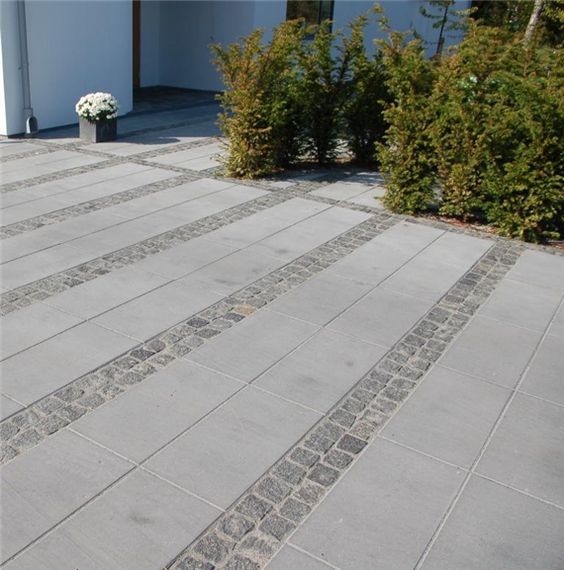 an outdoor patio with stone steps and shrubbery in the foreground, next to a white building