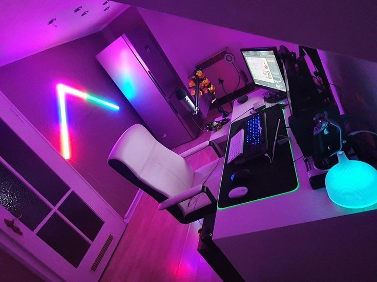 a desk with a chair, laptop and computer on it in a room lit up by neon lights