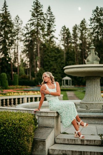 a woman is sitting on some steps in front of a fountain and looking at the camera