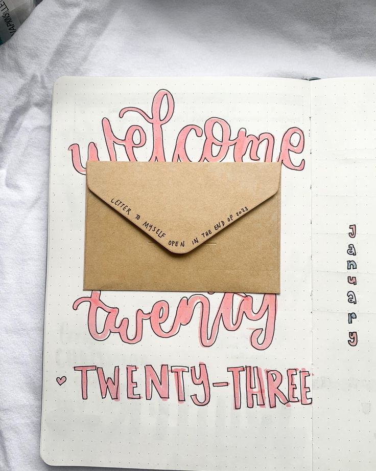 an open notebook with a brown envelope and pink lettering on the cover that says welcome twenty - three