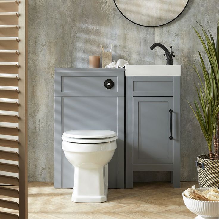 a white toilet sitting next to a sink in a bathroom under a round mirror on the wall