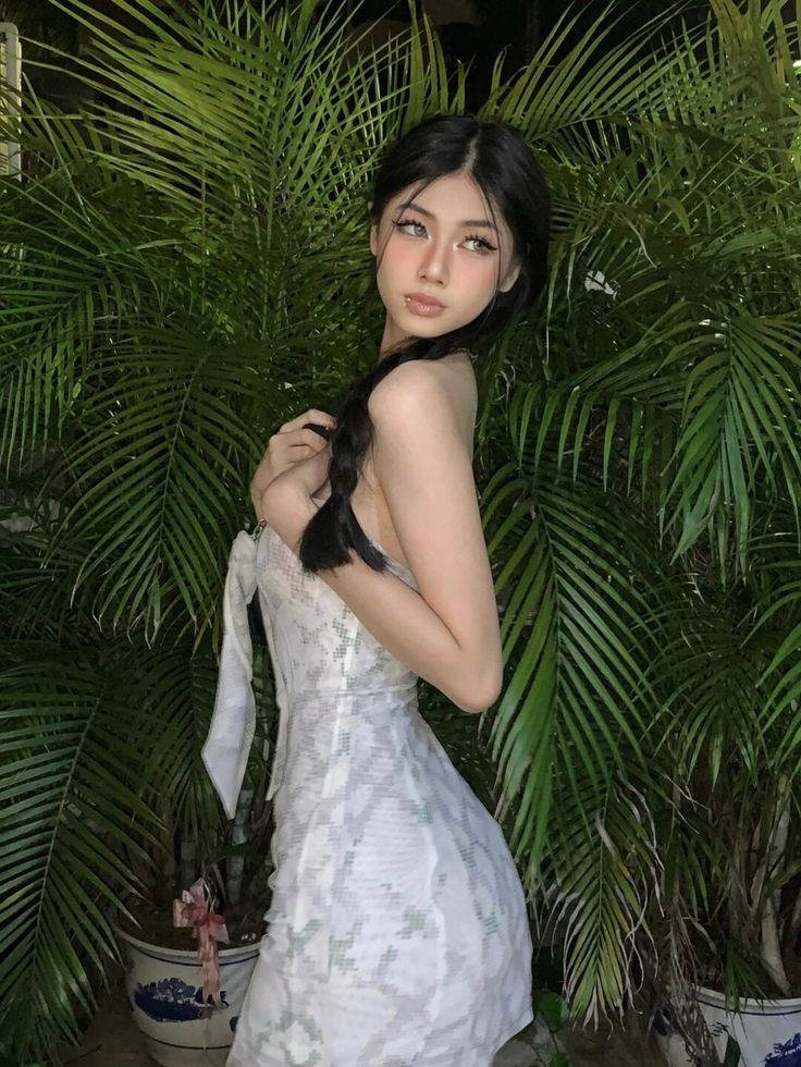 a woman in a white dress standing next to a palm tree