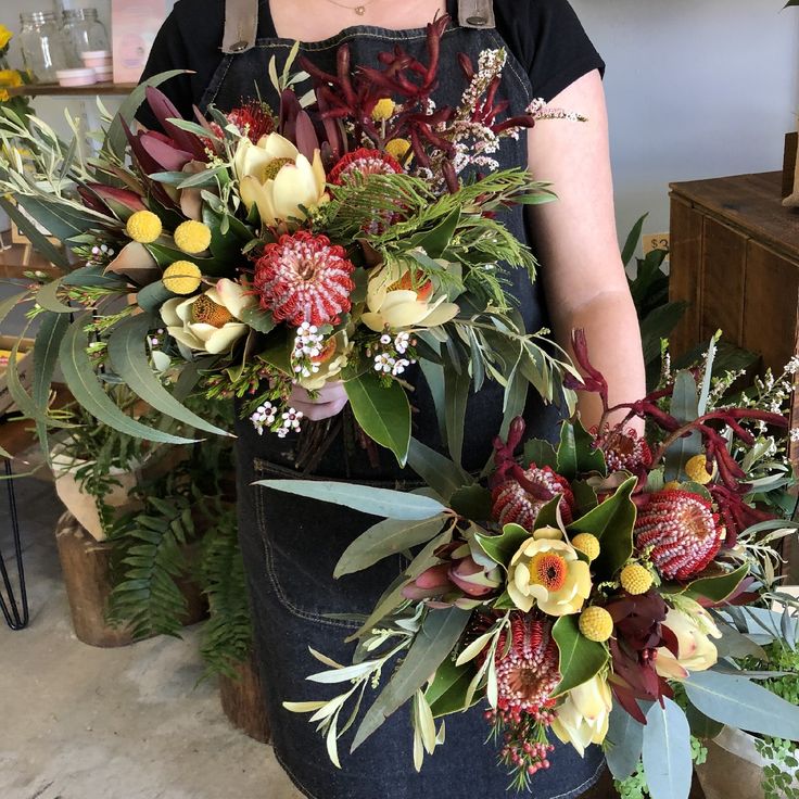 a woman in an apron is holding a large bouquet of flowers and greenery on the table