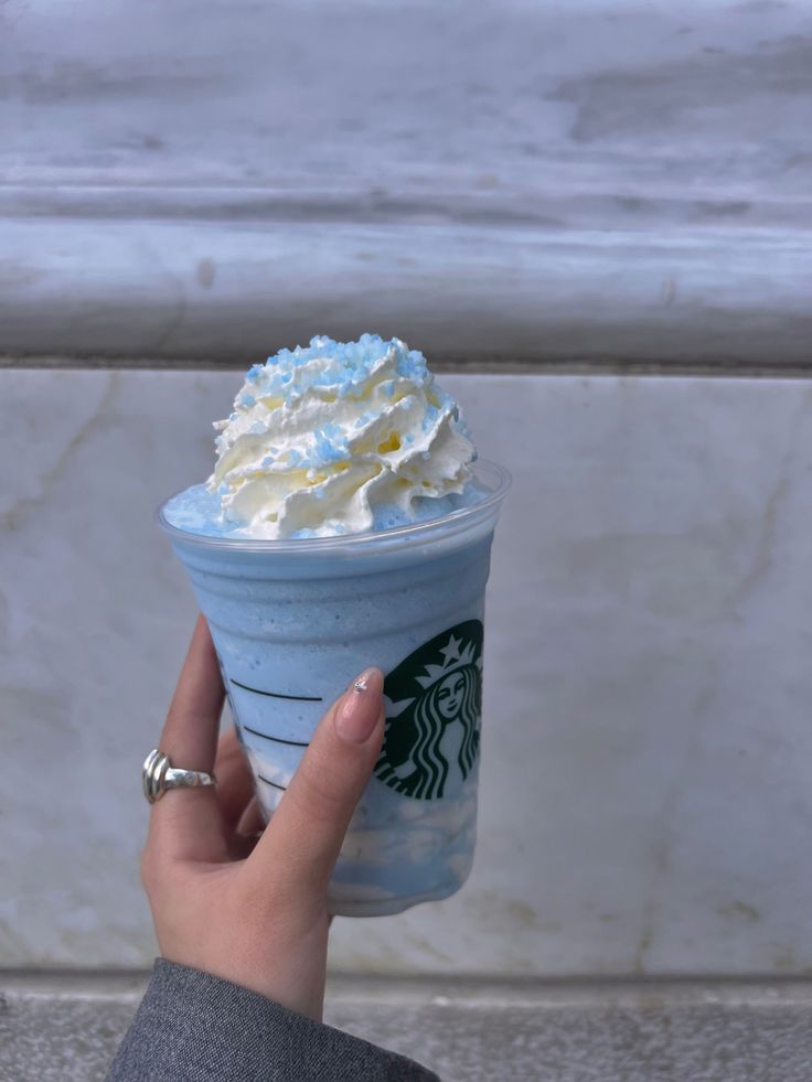 a starbucks cup with whipped cream on top is held up by a woman's hand