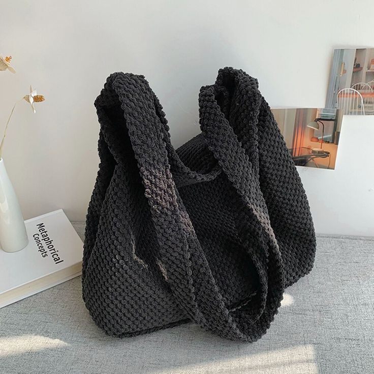 a black knitted bag sitting on top of a table next to a vase with flowers