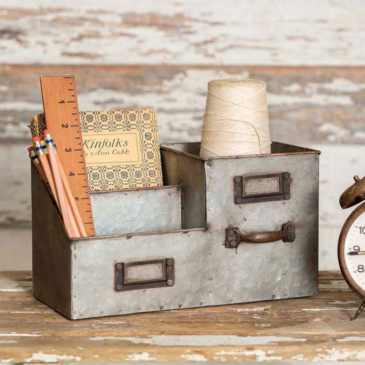 an alarm clock and some books in a metal box on a wooden table next to a white painted wall