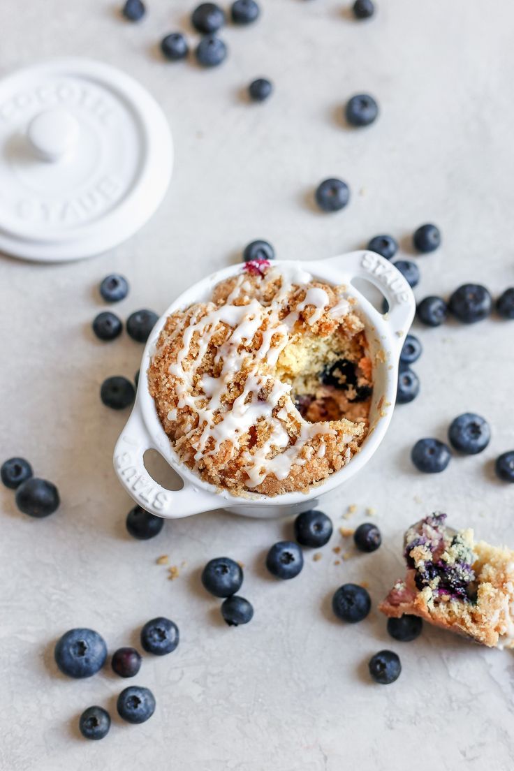 blueberry cobbler in a white bowl with a bite taken out of it and fresh blueberries scattered around