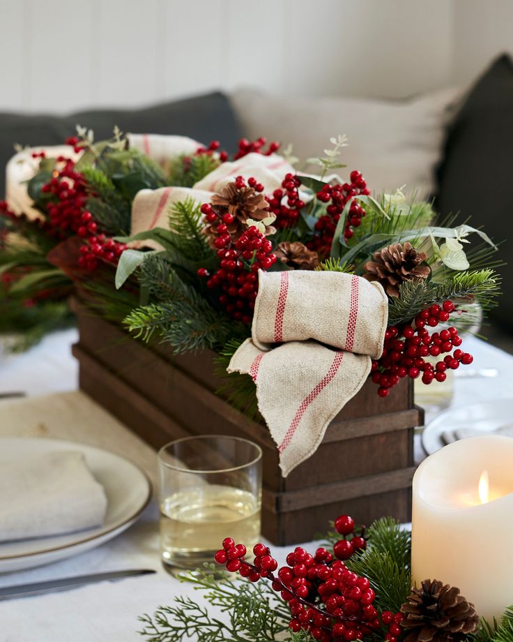 a christmas centerpiece with red berries, pine cones and greenery in a wooden box