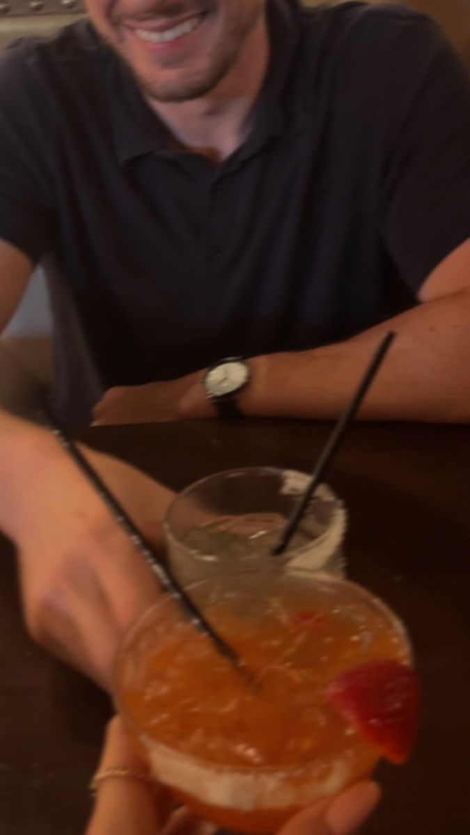 a man sitting at a table with a drink in front of him and smiling for the camera